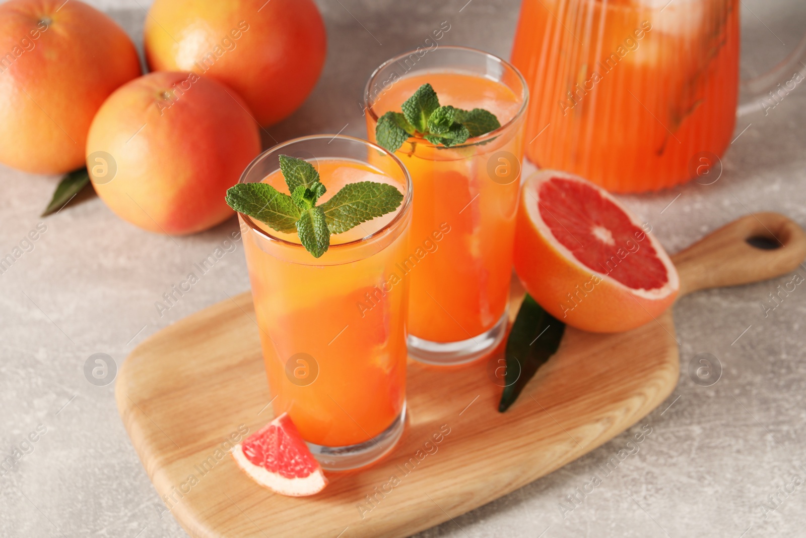 Photo of Tasty freshly made grapefruit juice, fruits and mint on light grey table