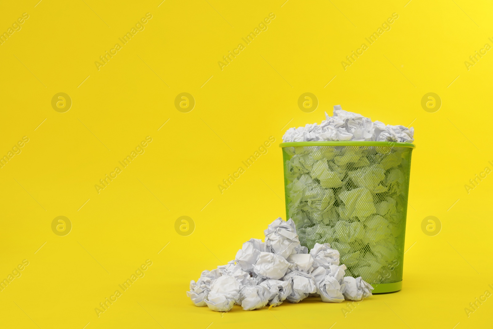 Photo of Metal bin with crumpled paper on color background, space for text