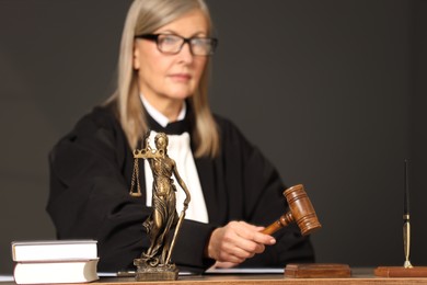 Photo of Judge striking mallet at wooden table, selective focus. Figure of Lady Justice indoors