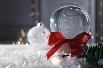 Photo of Christmas glass globe with artificial snow against blurred background. Space for text