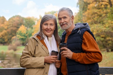 Photo of Affectionate senior couple with cups of coffee in autumn park