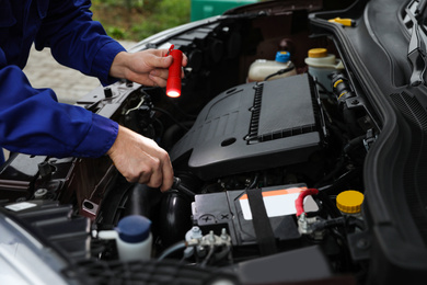 Mechanic with flashlight fixing car outdoors, closeup