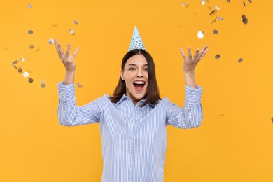 Photo of Happy young woman in party hat near flying confetti on yellow background