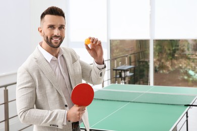 Photo of Businessman with tennis racket and ball near ping pong table in office. Space for text