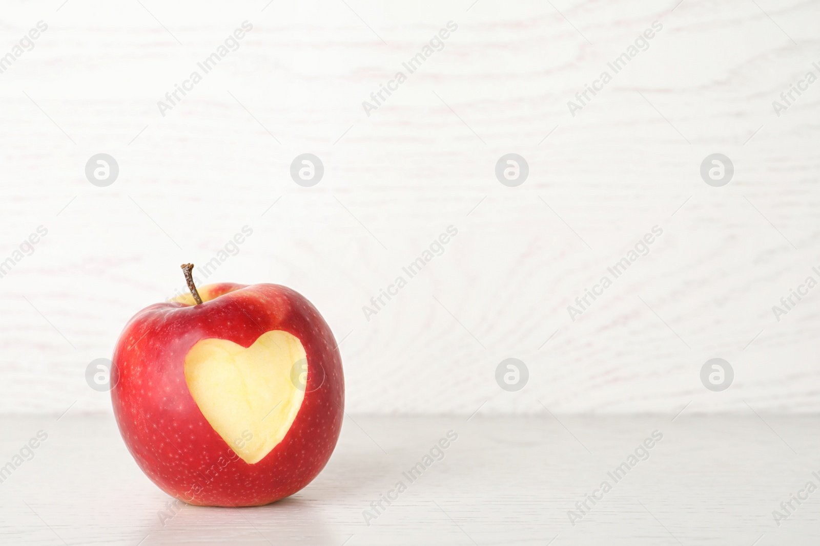 Photo of Red apple with carved heart on light background. Space for text