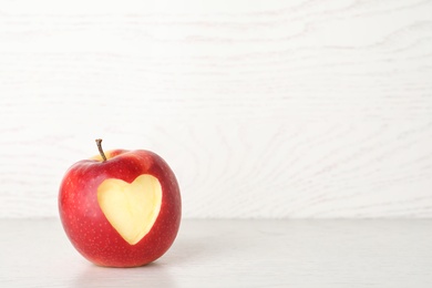 Photo of Red apple with carved heart on light background. Space for text