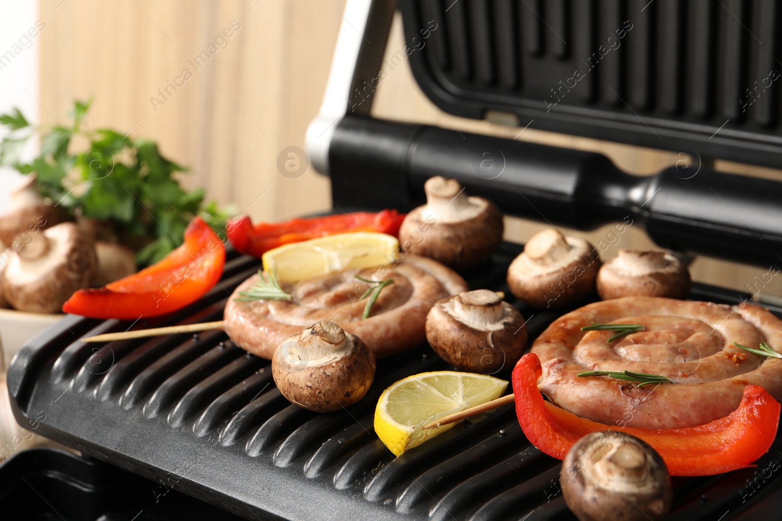 Photo of Electric grill with homemade sausages, mushrooms and bell pepper on table, closeup