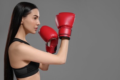 Photo of Beautiful woman in boxing gloves training on grey background. Space for text