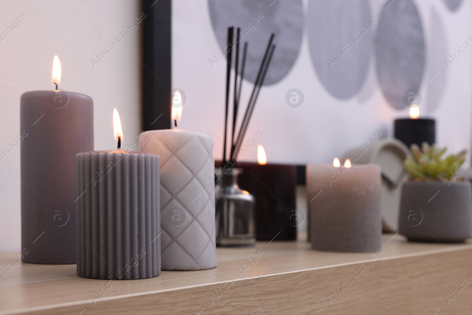 Photo of Burning candles and air freshener on wooden shelf indoors