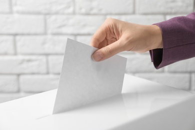 Photo of Woman putting her vote into ballot box against brick wall, closeup