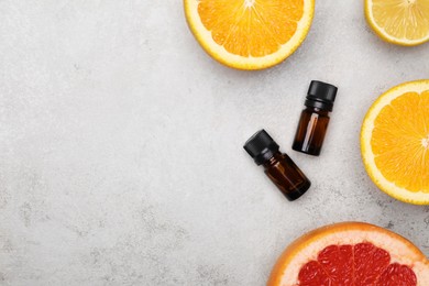 Photo of Bottles of citrus essential oils and fresh fruits on light table, flat lay. Space for text