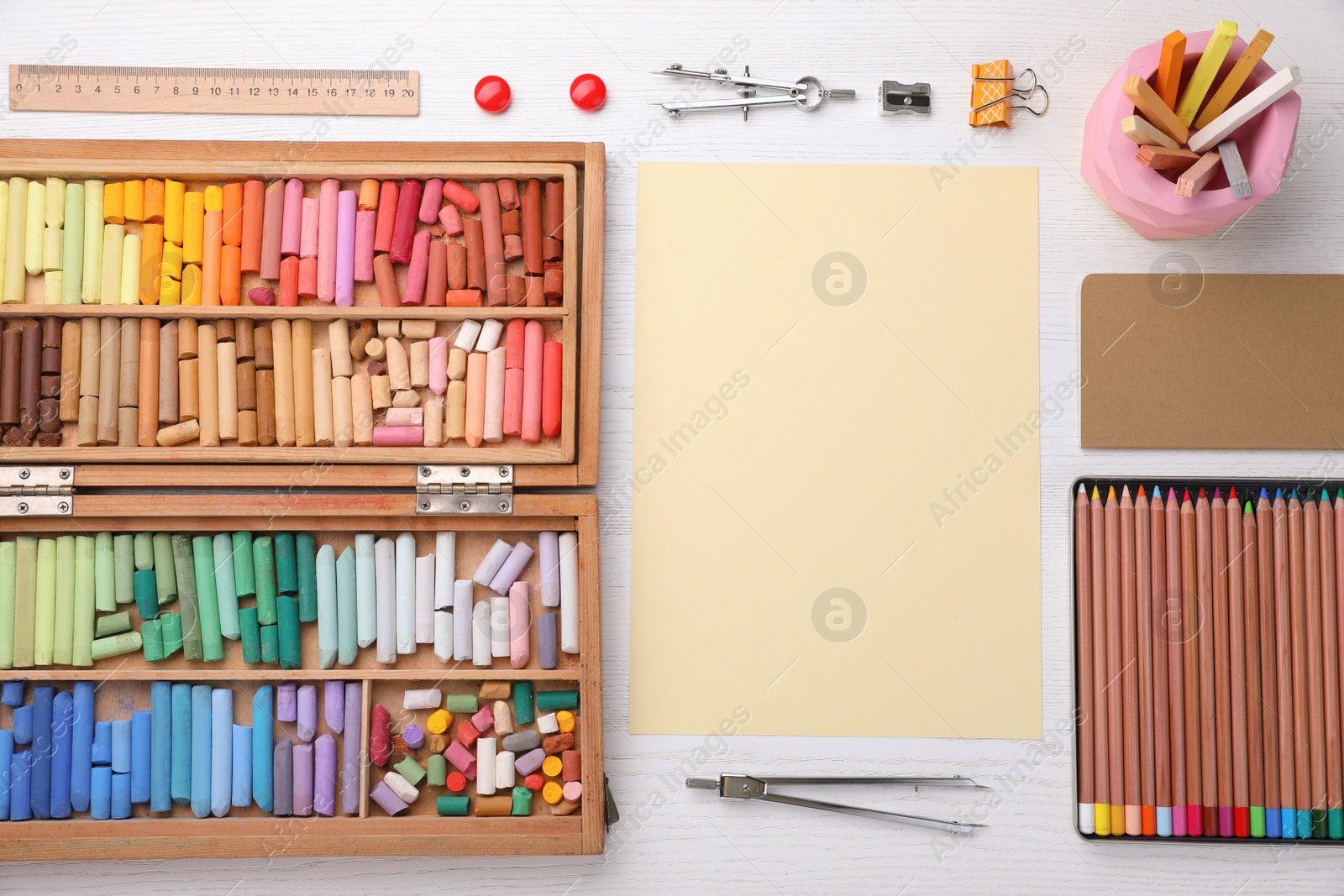Photo of Layout with blank paper, soft pastels and other drawing supplies on white wooden table at artist's workplace, top view. Space for design