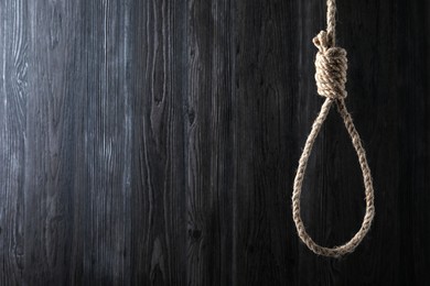 Photo of Tied rope noose against dark wooden background. Space for text