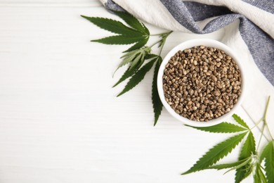 Photo of Organic hemp seeds and leaves on white wooden table, flat lay. Space for text