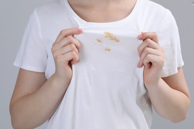 Photo of Woman showing stain on her t-shirt against light grey background, closeup