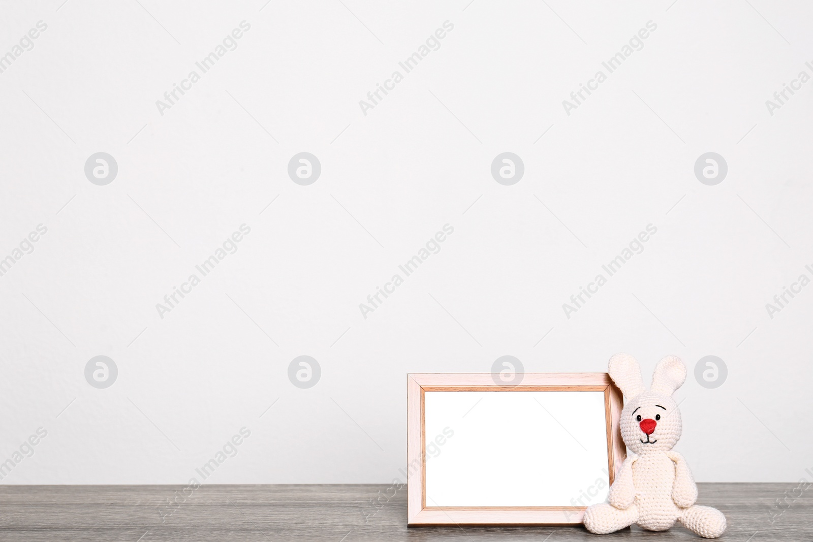 Photo of Photo frame and adorable toy bunny on table against light background, space for text. Child room elements