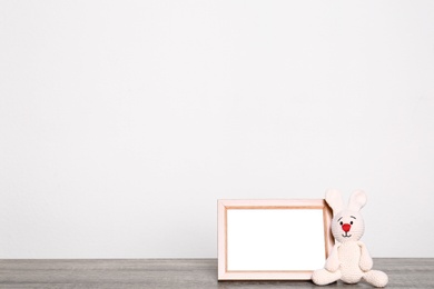 Photo of Photo frame and adorable toy bunny on table against light background, space for text. Child room elements