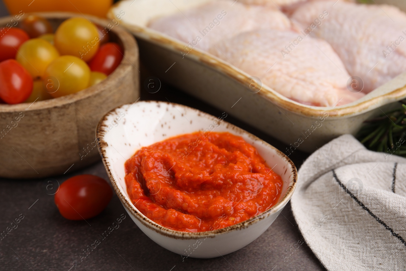 Photo of Fresh marinade, raw chicken and tomatoes on brown table, closeup