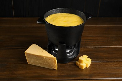 Fondue pot with melted cheese and pieces at wooden table