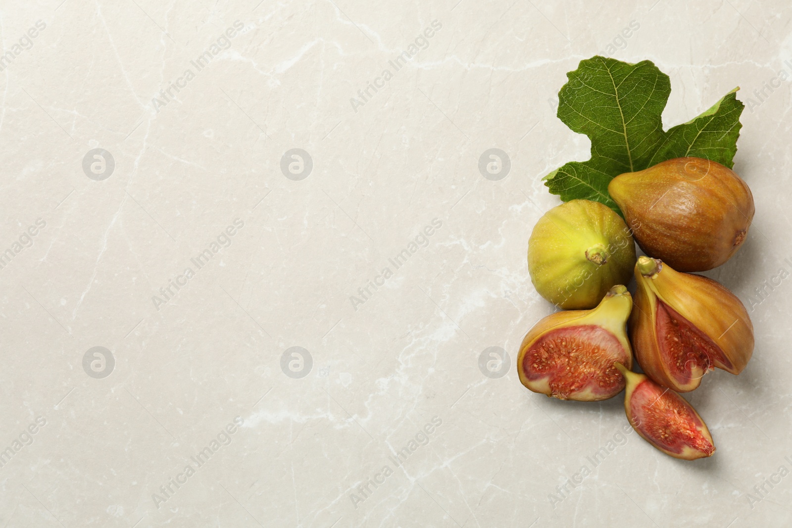 Photo of Tasty raw figs and green leaf on light grey marble table, flat lay. Space for text