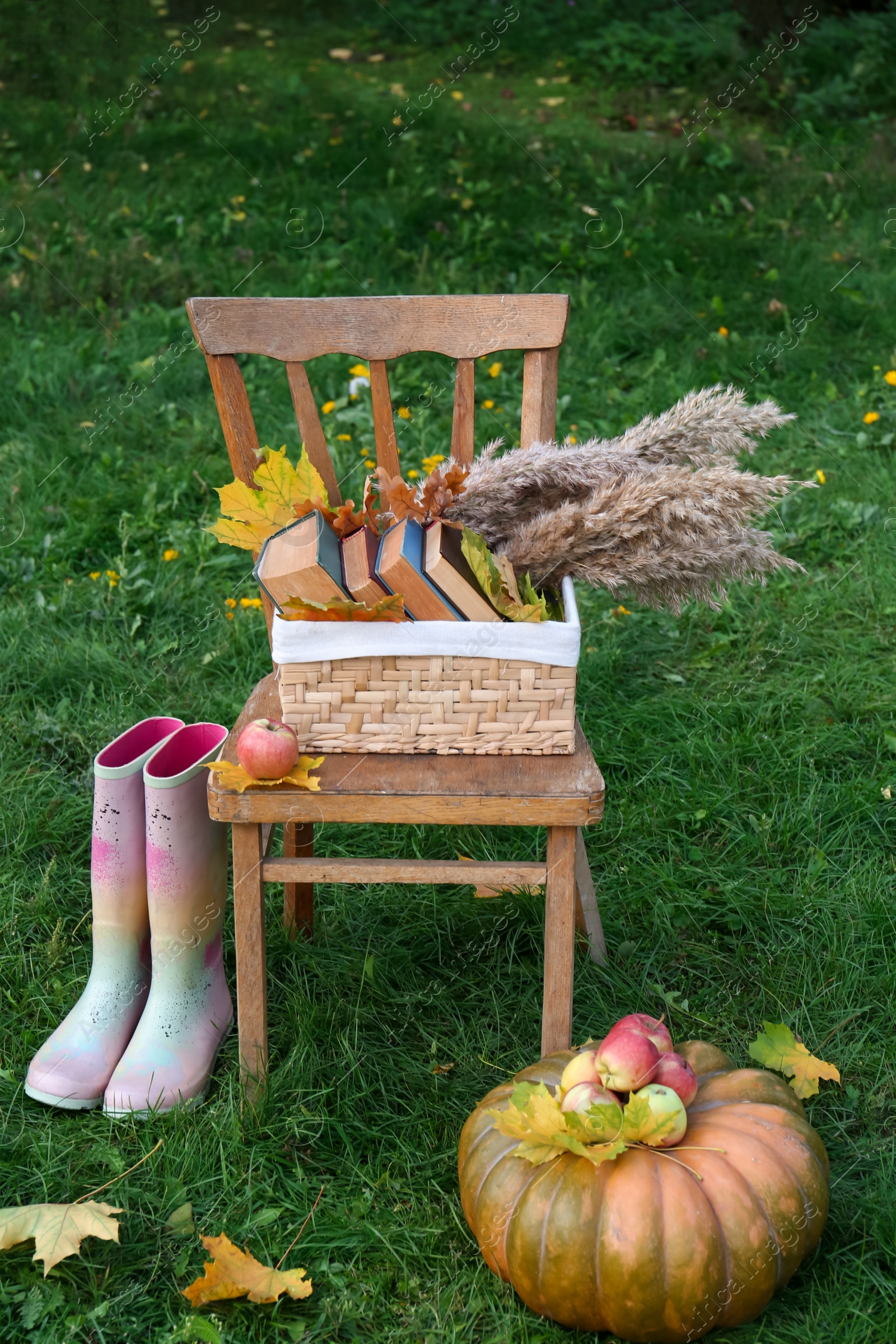 Photo of Rubber boots, chair, pumpkin and apples on green grass outdoors. Autumn atmosphere