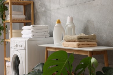Photo of Soft towels, detergents, bench, houseplant and washing machine indoors