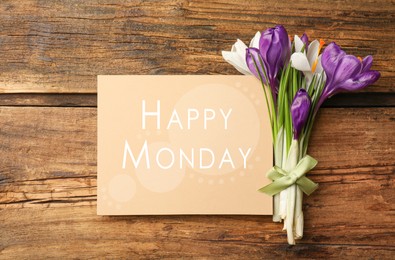 Image of Beautiful spring crocus flowers and card with phrase Happy Monday on wooden table, flat lay 