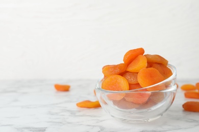 Bowl with apricots on marble table, space for text. Dried fruit as healthy food