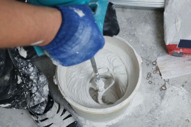 Photo of Professional worker mixing plaster in bucket indoors, closeup