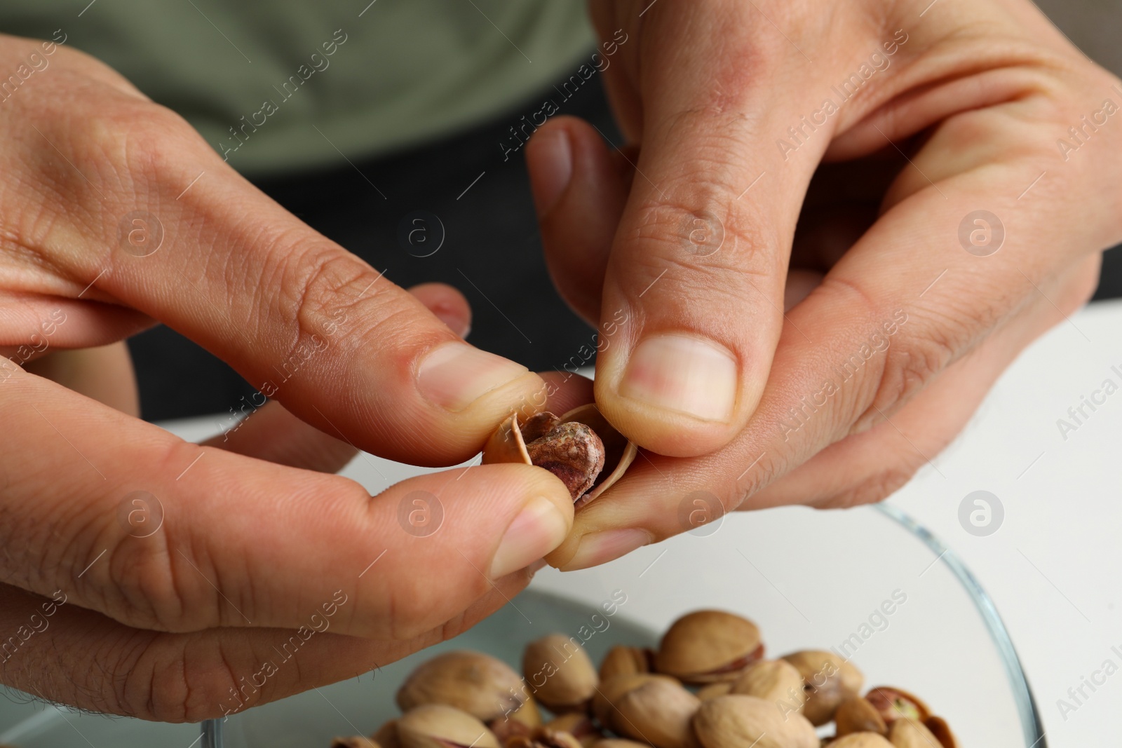 Photo of Woman opening tasty roasted pistachio nut at white table, closeup