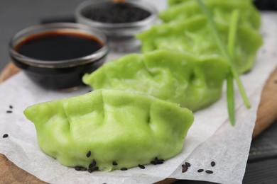 Photo of Delicious green dumplings (gyozas), soy sauce and sesame seeds on table, closeup