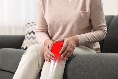 Image of Arthritis symptoms. Woman suffering from pain in her knee on sofa indoors, closeup