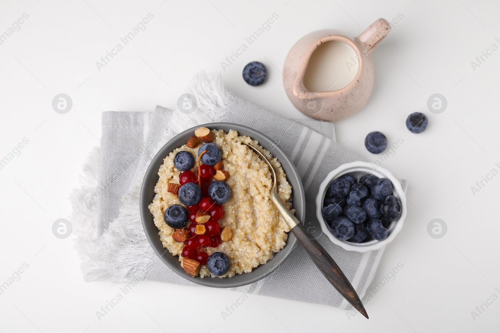 Photo of Bowl of delicious cooked quinoa with almonds, cranberries and blueberries on white background, flat lay