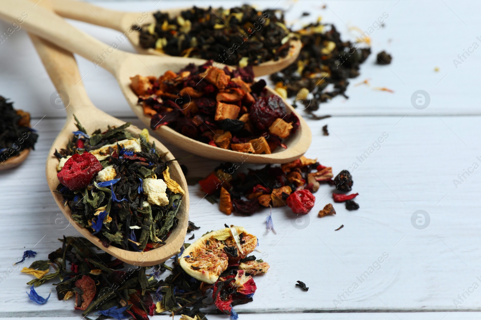 Photo of Spoons with dried herbal tea leaves and fruits on white wooden table, closeup. Space for text