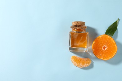 Photo of Aromatic tangerine essential oil in bottle and citrus fruit on light blue table, top view. Space for text