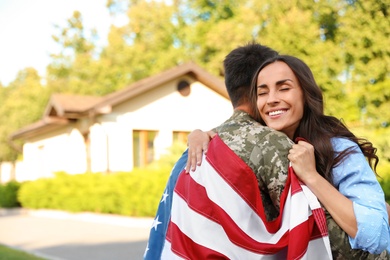 Man in military uniform with American flag hugging his wife outdoors