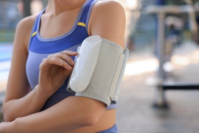 Woman checking blood pressure with modern monitor after training against blurred background, closeup. Space for text