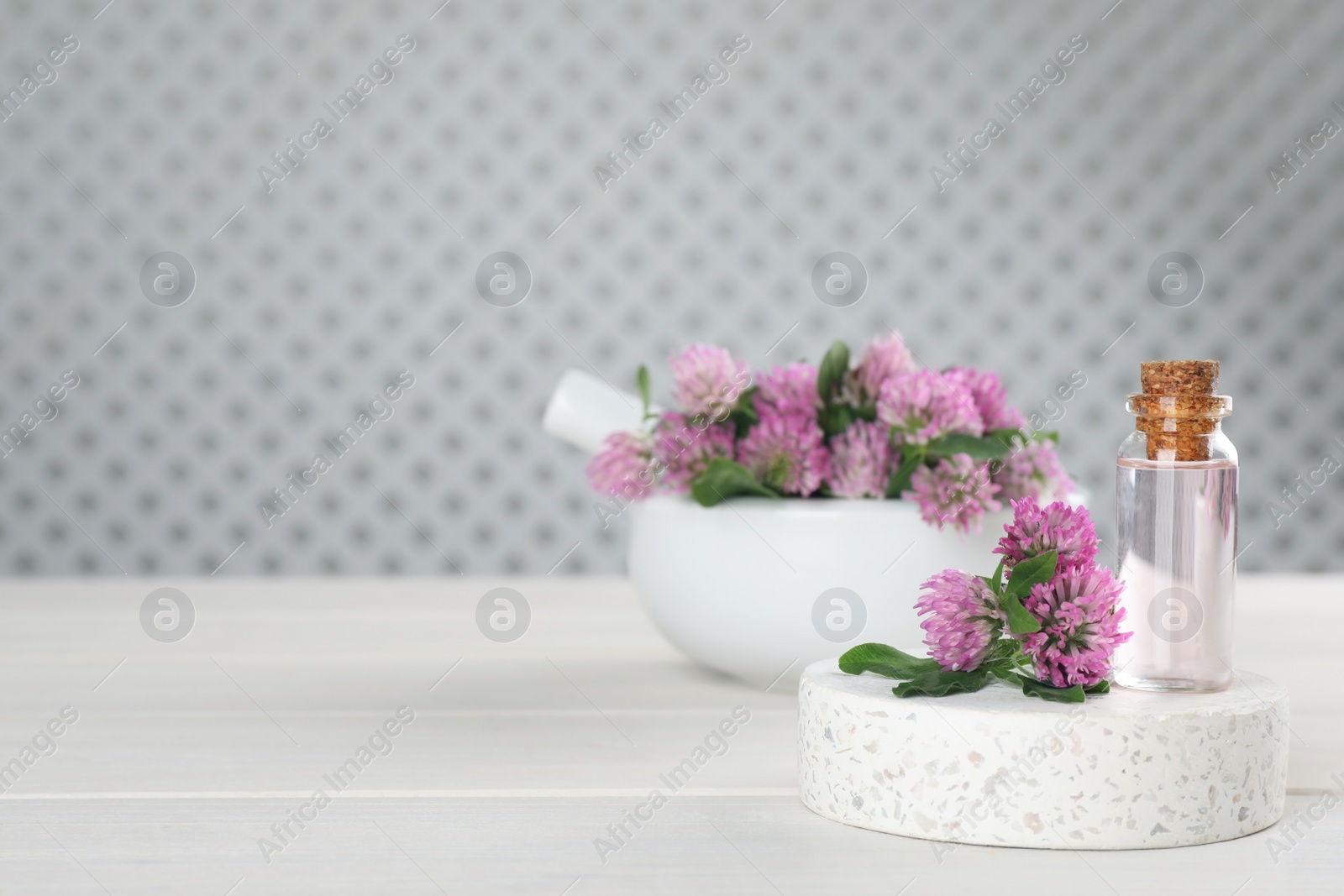 Photo of Beautiful clover flowers and bottle of essential oil on white wooden table. Space for text