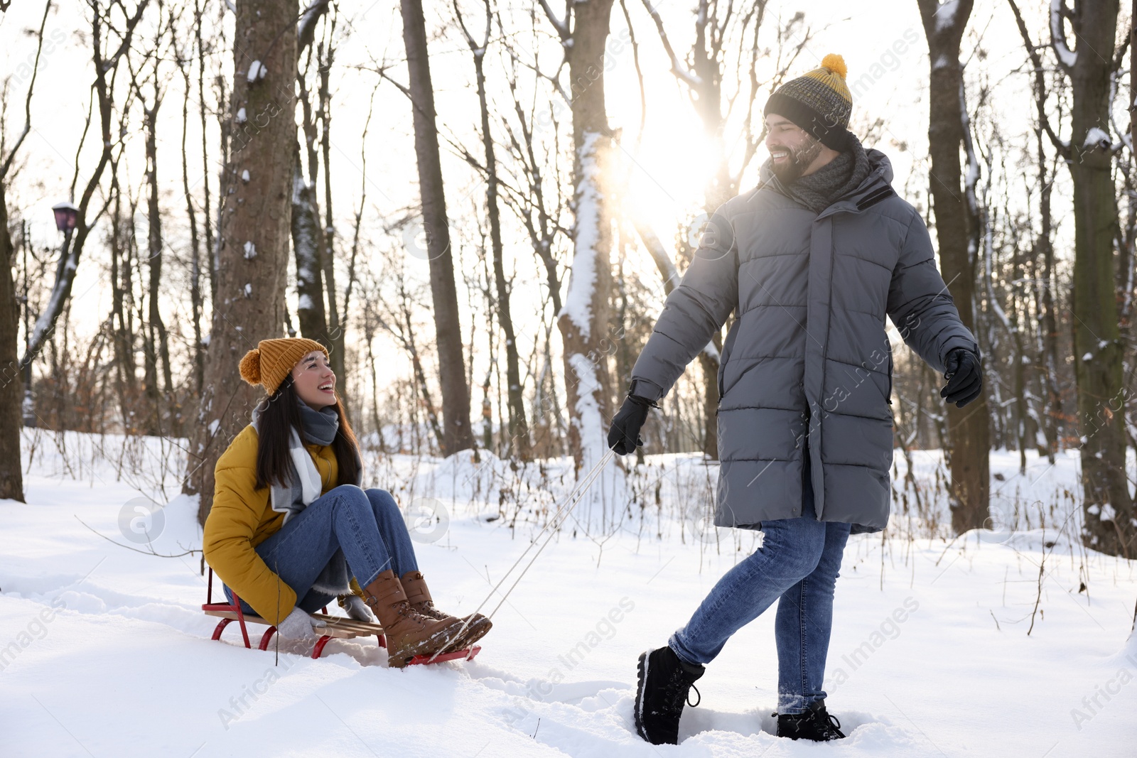 Photo of Happy young man pulling his girlfriend in sleigh outdoors on winter day