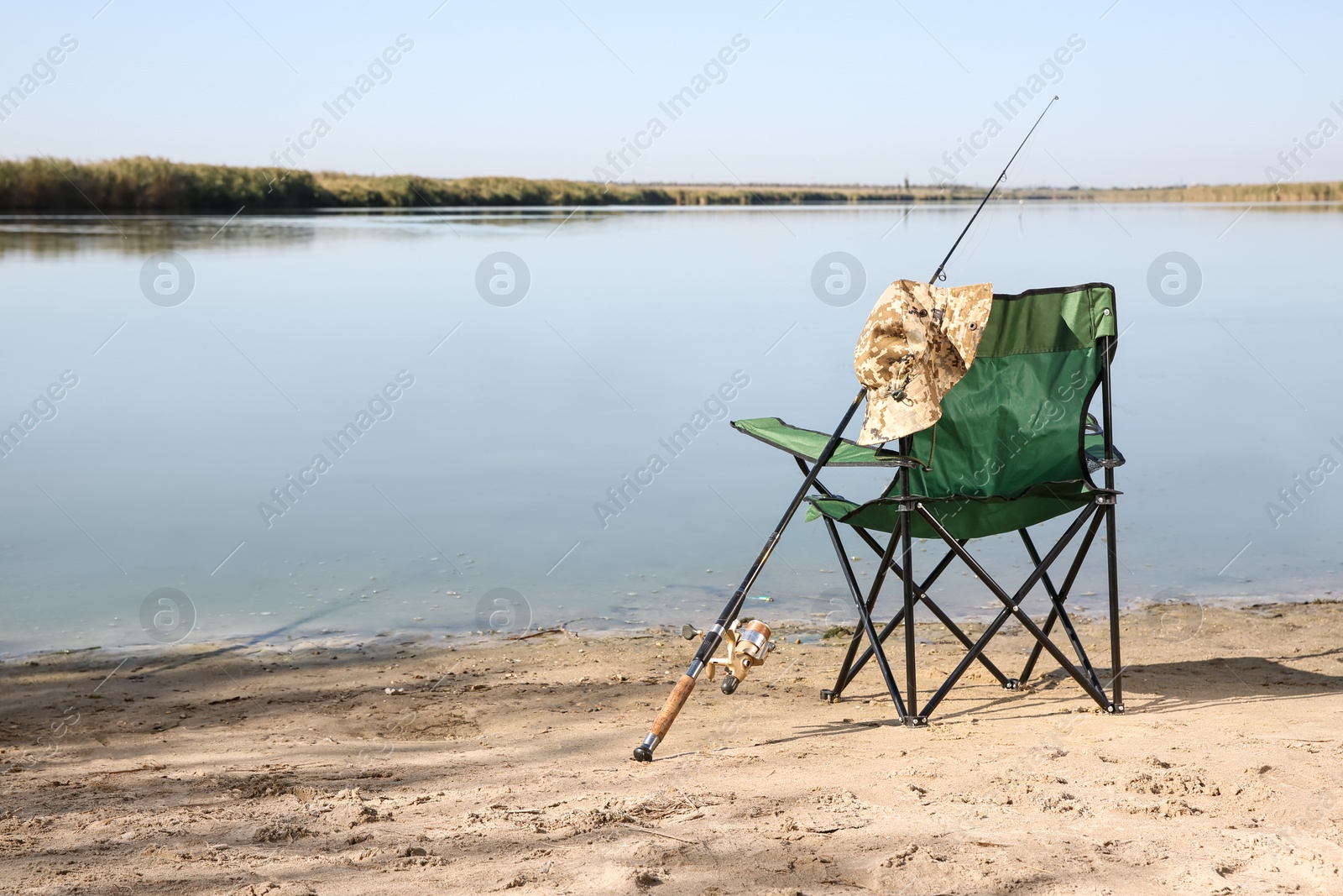 Photo of Camping chair and fishing rod at riverside on sunny day. Space for text