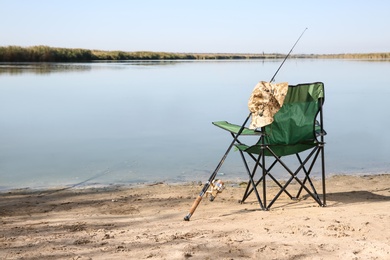 Photo of Camping chair and fishing rod at riverside on sunny day. Space for text