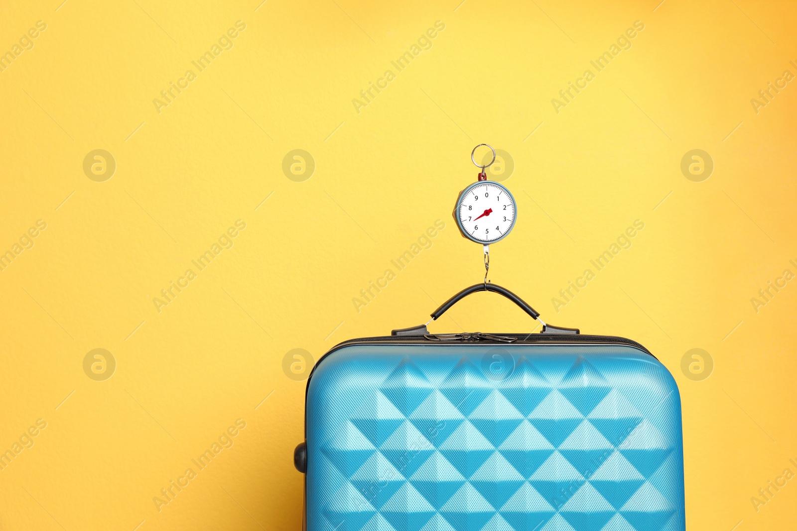 Photo of Modern suitcase and hanging scales against color background, space for text