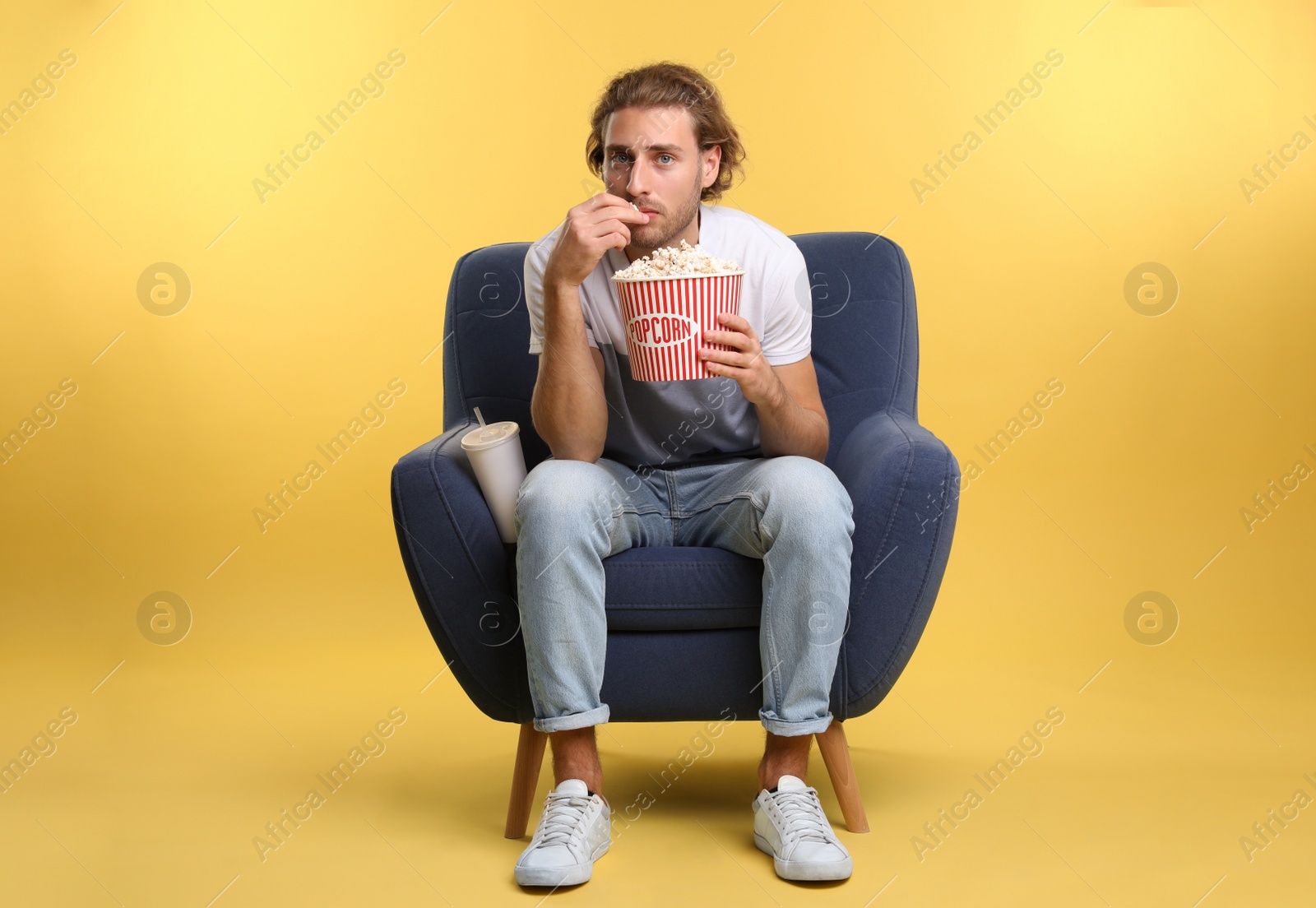 Photo of Man with popcorn and beverage sitting in armchair during cinema show on color background