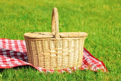 Photo of Picnic basket with checkered tablecloth on green grass outdoors