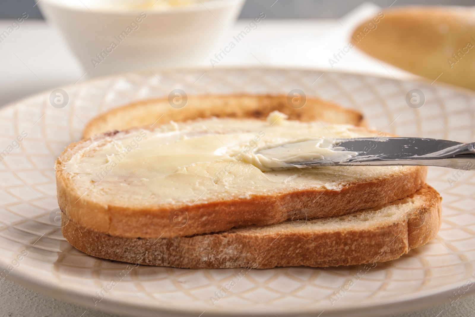 Photo of Spreading tasty butter onto slice of bread with knife on plate, closeup