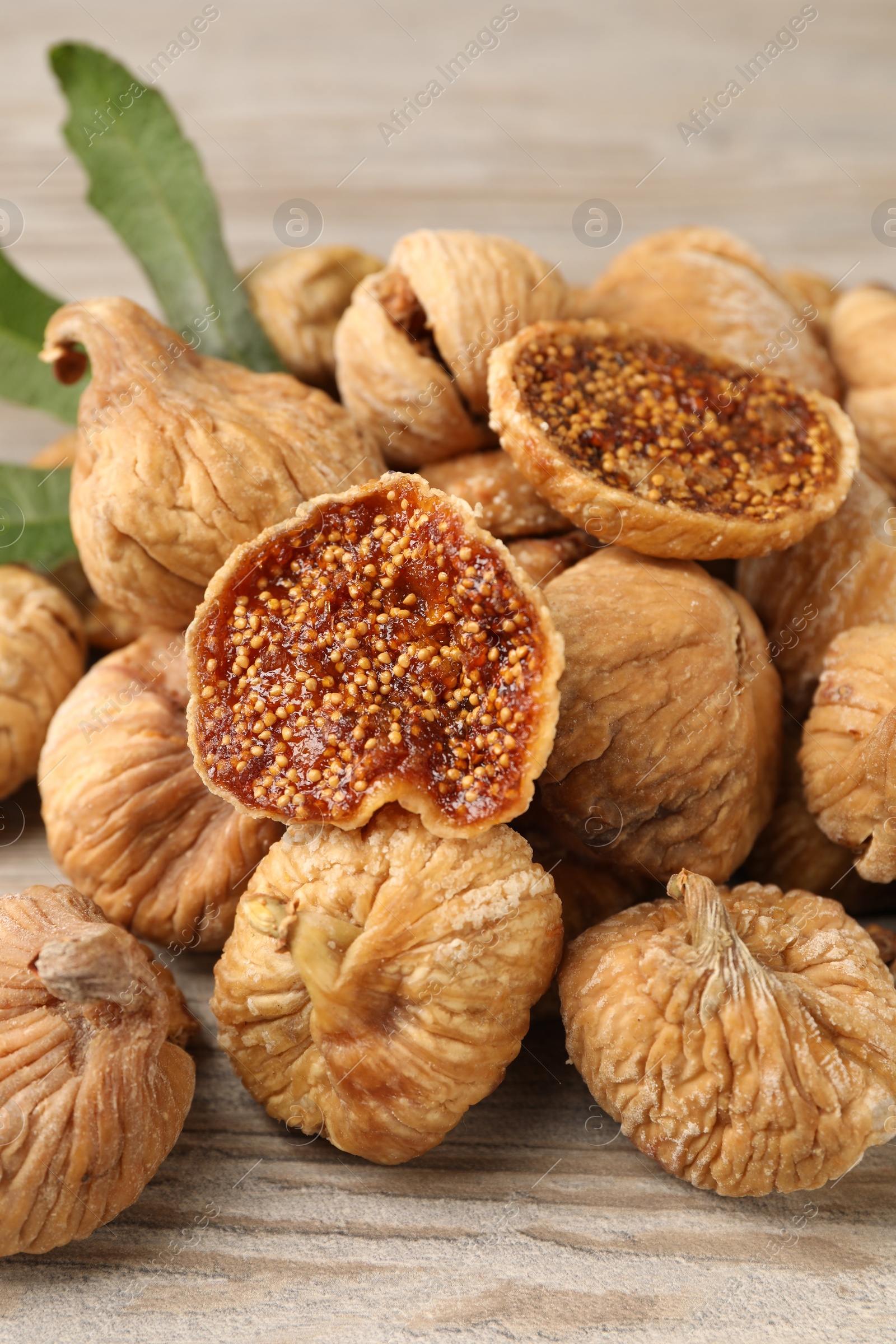 Photo of Tasty dried figs and green leaf on light wooden table, closeup