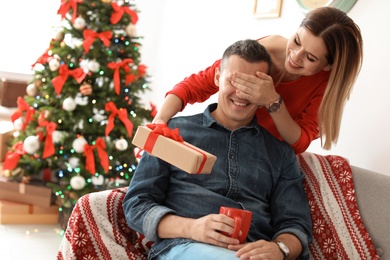 Young woman surprising her boyfriend with Christmas gift at home