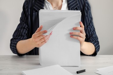 Woman stacking documents at white wooden table in office, closeup