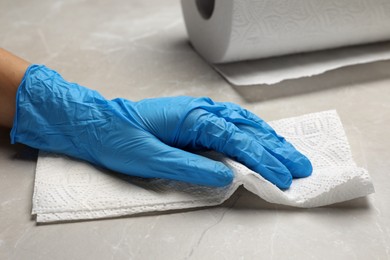 Photo of Woman in glove cleaning light grey table with paper towel, closeup