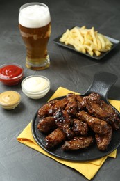 Photo of Tasty roasted chicken wings, sauces, french fries and glass of beer on black table